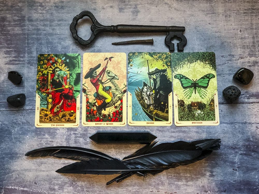 Four tarot cards laid out between black stones, a black key, crystals, and crow feathers.