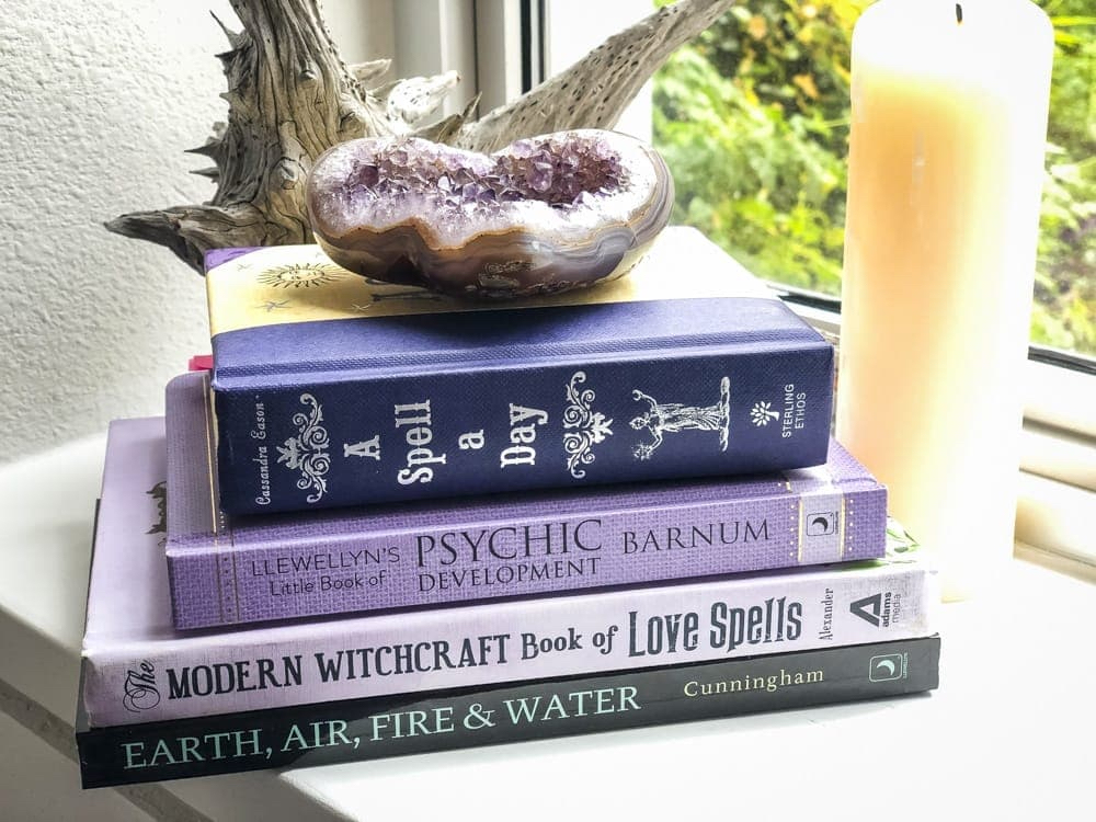 A stack of witchcraft books with a candle and an amethyst crystal specimen 