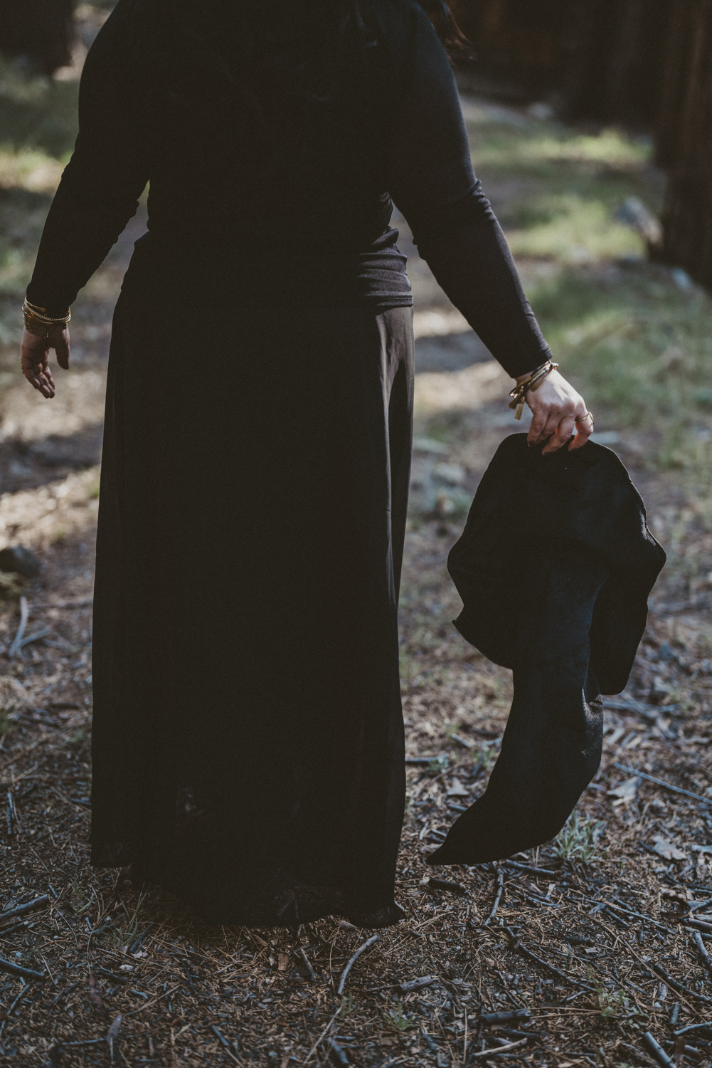 An image of elena in a black dress walking away, with a witch hat trailing behind her